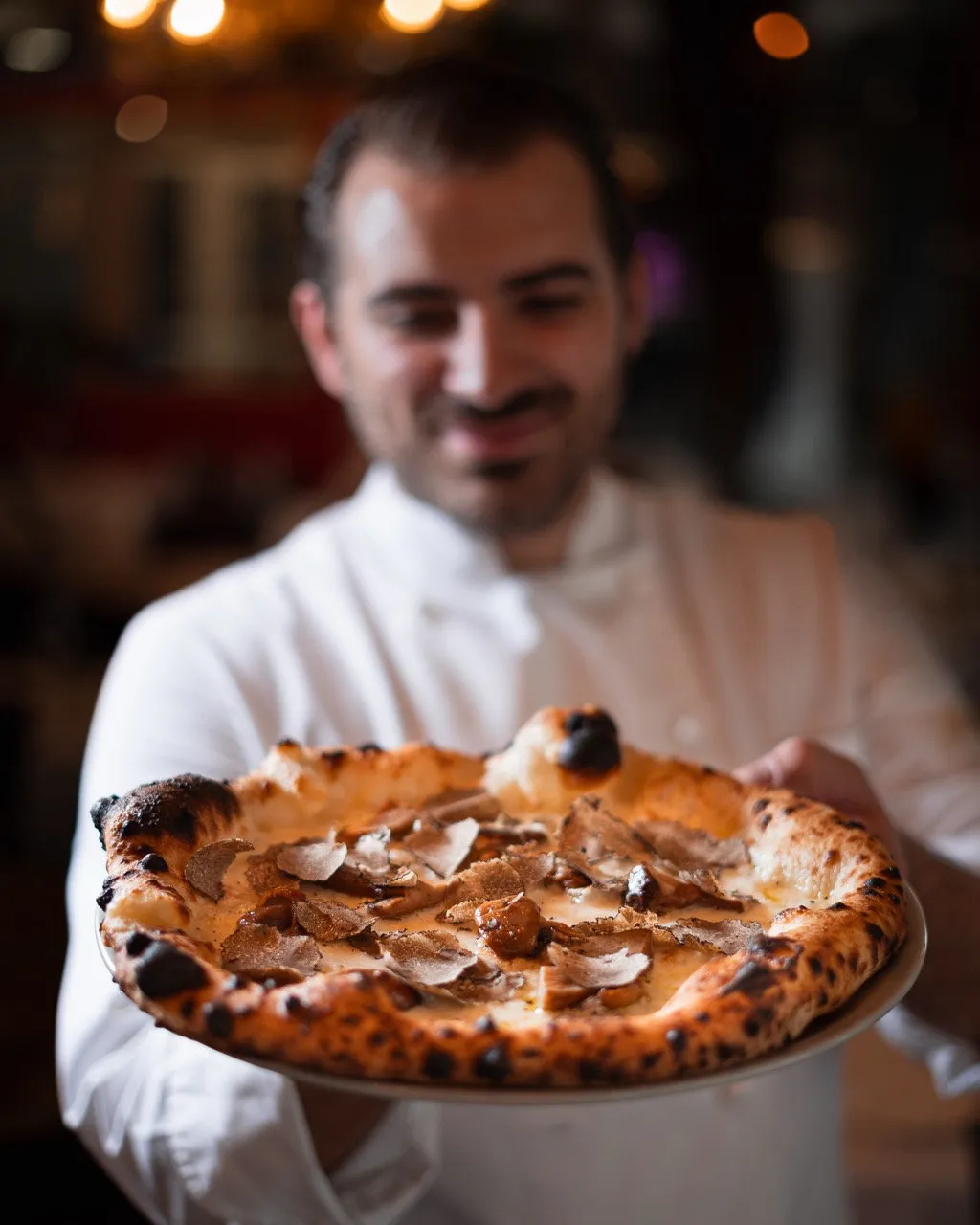 Italienischer Kellner bringt eine frisch gebackene Steinofenpizza zu Gästen an einem freundlich gedeckten Tisch