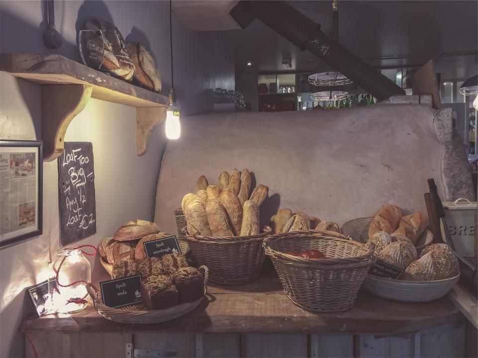 Frische Brote und Baguettes in Körben auf einer Holztheke vor einem Steinofen