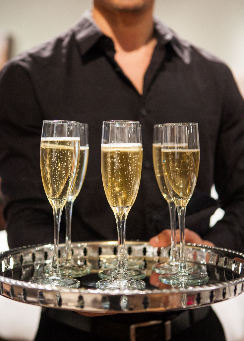 Servicekraft trägt ein Silbertablett mit gefüllten Champagnergläsern