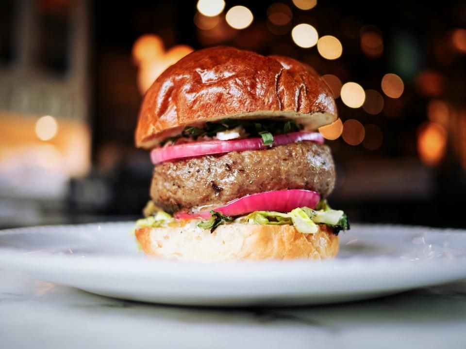 Burger mit Brioche-Bun, roten Zwiebeln und Salat auf einem weissen Teller